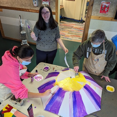 Catherine smiles while Riley and Spencer continue turning the umbrella into a flower